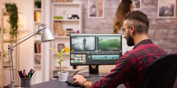 Back view of creative filmmaker working on a movie on laptop. Girlfriend in the background.